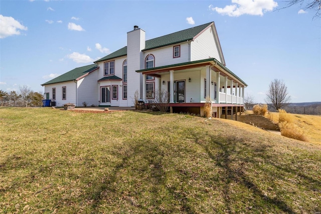 back of property featuring a porch, a lawn, and a chimney