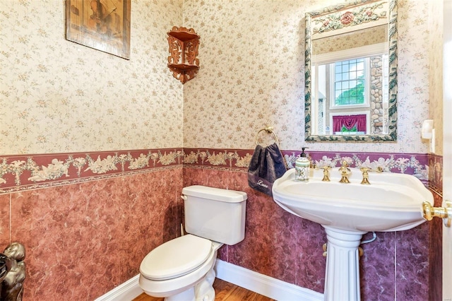 half bathroom with toilet, wood finished floors, and wallpapered walls
