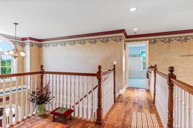 hall with an upstairs landing, a notable chandelier, ornamental molding, and wood-type flooring