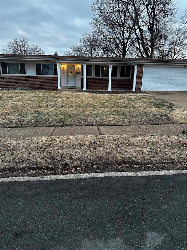 view of front of home with a front lawn, covered porch, concrete driveway, an attached garage, and brick siding