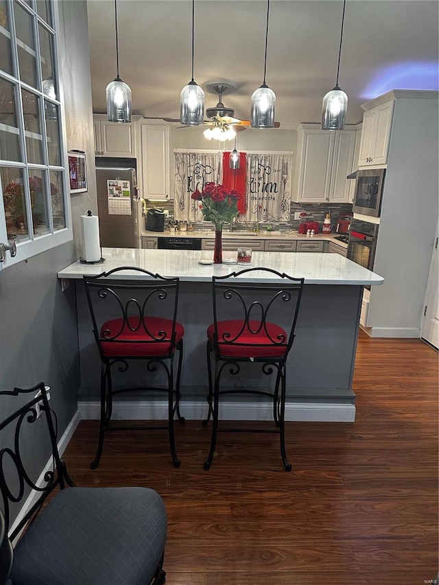 kitchen with dark wood-type flooring, black appliances, a kitchen breakfast bar, backsplash, and a peninsula