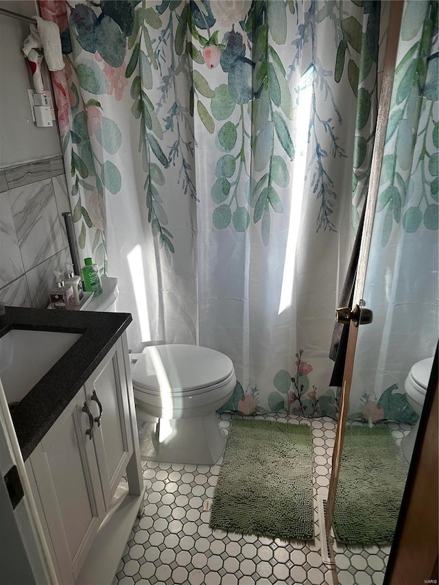 full bath with toilet, a shower with shower curtain, tile walls, tile patterned flooring, and vanity