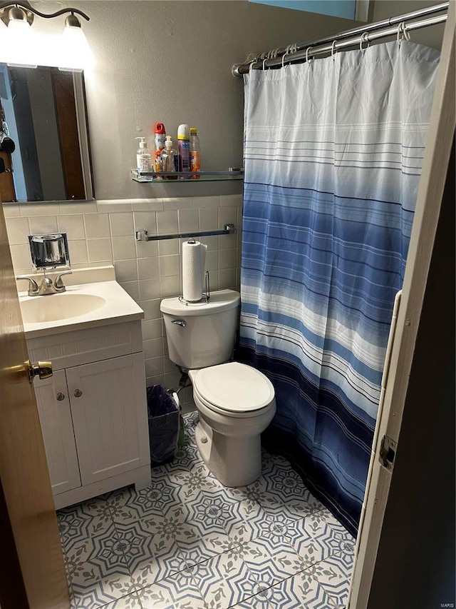 bathroom with tile patterned flooring, a wainscoted wall, toilet, vanity, and tile walls