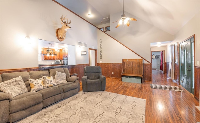 living area featuring high vaulted ceiling, a wainscoted wall, wood walls, dark wood-style flooring, and visible vents