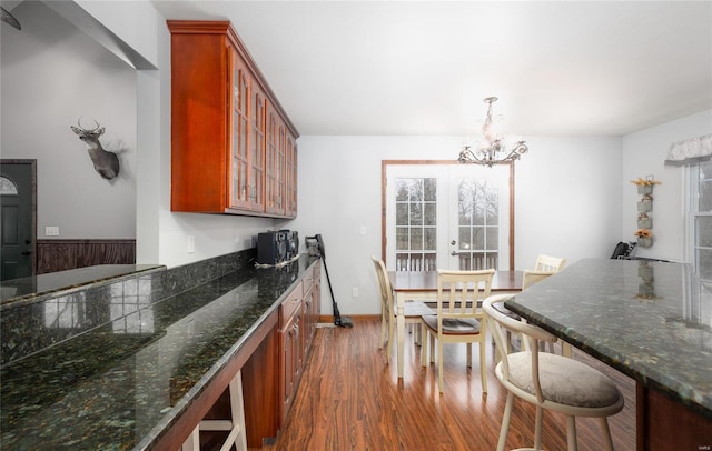 kitchen featuring dark wood-type flooring, a breakfast bar, brown cabinets, glass insert cabinets, and an inviting chandelier