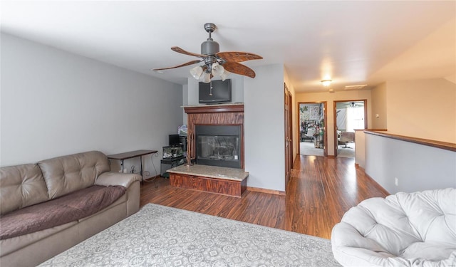 living room featuring visible vents, a ceiling fan, a glass covered fireplace, wood finished floors, and baseboards