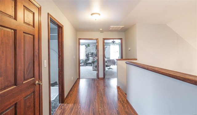 hallway with baseboards, visible vents, dark wood finished floors, and an upstairs landing