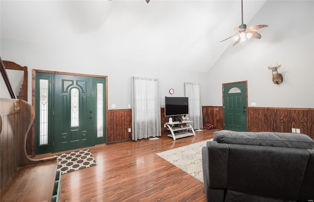 living room with a ceiling fan, wood walls, high vaulted ceiling, and wainscoting