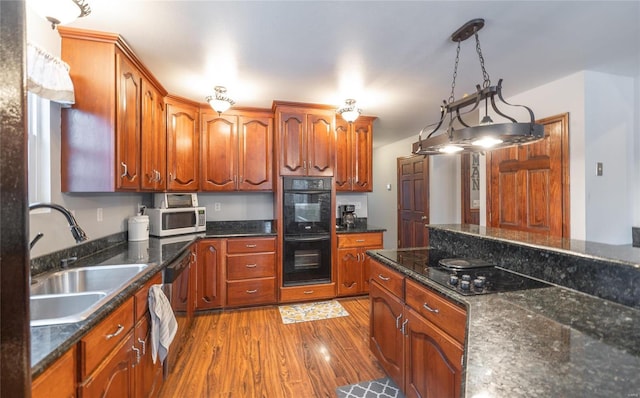 kitchen with brown cabinetry, black appliances, wood finished floors, a sink, and decorative light fixtures