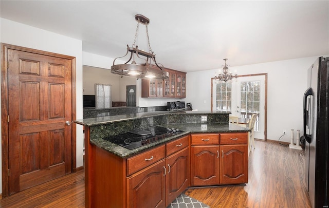 kitchen with a center island, a notable chandelier, glass insert cabinets, wood finished floors, and black appliances