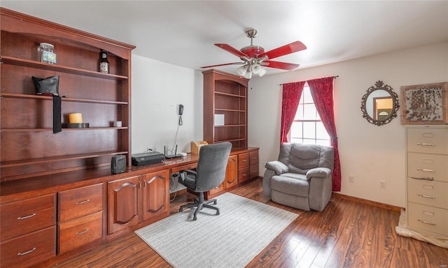 office space with built in desk, baseboards, a ceiling fan, and dark wood-style floors