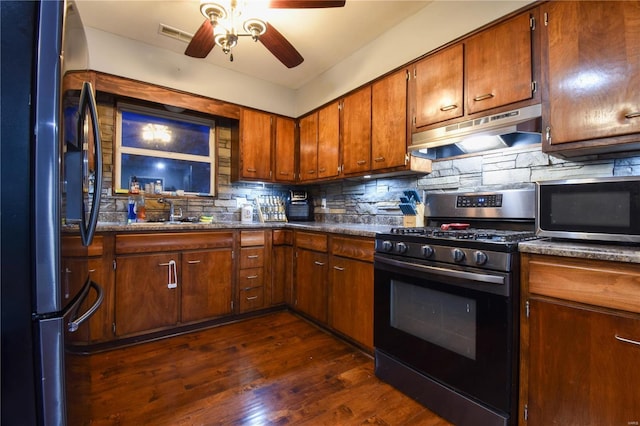 kitchen with dark wood-type flooring, under cabinet range hood, tasteful backsplash, appliances with stainless steel finishes, and ceiling fan