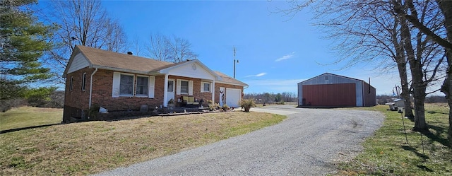 bungalow-style home featuring brick siding, gravel driveway, a front lawn, a garage, and an outbuilding