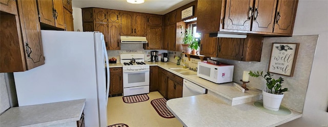 kitchen featuring under cabinet range hood, a sink, white appliances, brown cabinetry, and light countertops