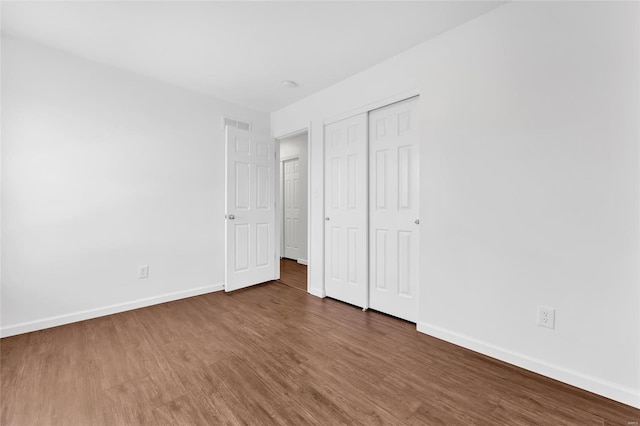 unfurnished bedroom with a closet, wood finished floors, and baseboards