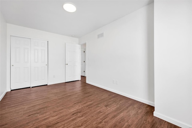 unfurnished bedroom with baseboards, visible vents, dark wood finished floors, and a closet