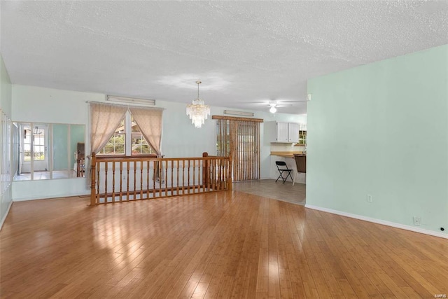 unfurnished living room featuring a textured ceiling, baseboards, hardwood / wood-style flooring, and a notable chandelier