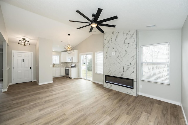 unfurnished living room with visible vents, baseboards, lofted ceiling, a fireplace, and light wood-style floors