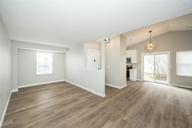 unfurnished living room featuring vaulted ceiling, wood finished floors, and baseboards