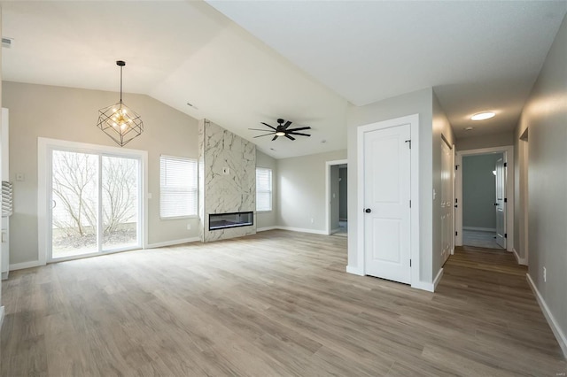 unfurnished living room featuring a high end fireplace, baseboards, light wood-style floors, and vaulted ceiling