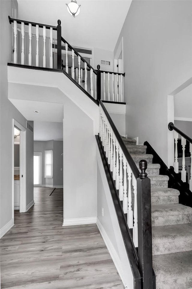 stairs featuring visible vents, a high ceiling, baseboards, and wood finished floors