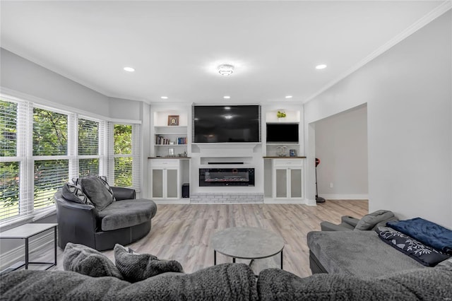 living area with built in shelves, recessed lighting, light wood-style floors, a glass covered fireplace, and crown molding