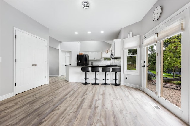 kitchen with white cabinets, decorative backsplash, dark countertops, a breakfast bar, and freestanding refrigerator