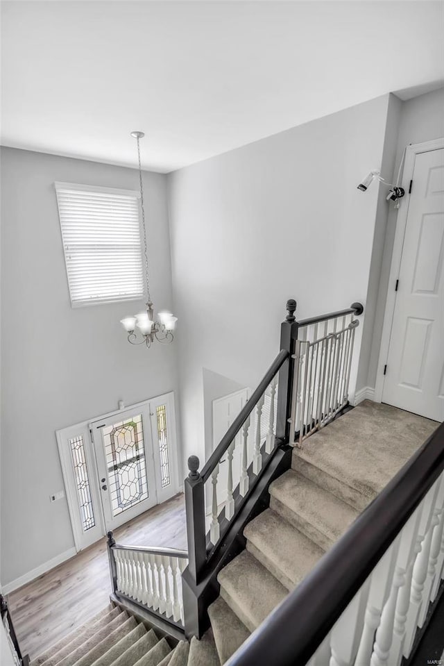 stairs with a chandelier, plenty of natural light, wood finished floors, and a towering ceiling