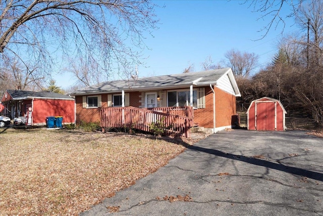 view of front of property with a storage shed, an outbuilding, brick siding, and aphalt driveway