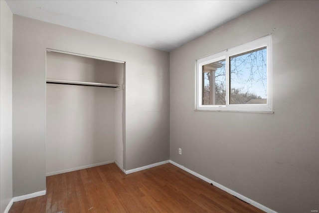 unfurnished bedroom featuring wood finished floors, a closet, and baseboards