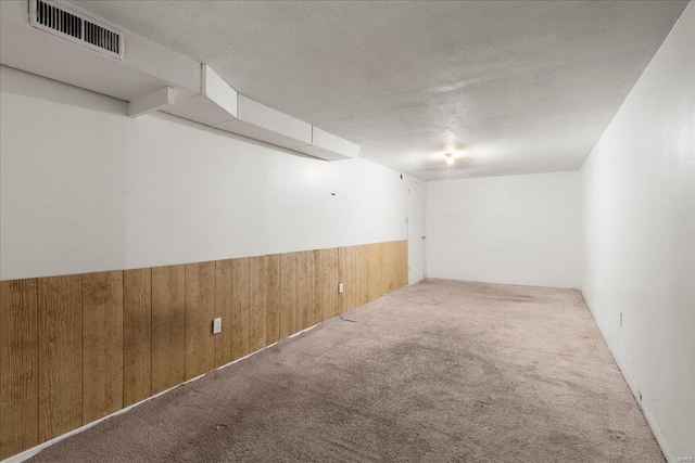 carpeted empty room featuring a textured ceiling, visible vents, wood walls, and wainscoting