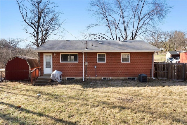 back of house featuring brick siding, a lawn, and fence