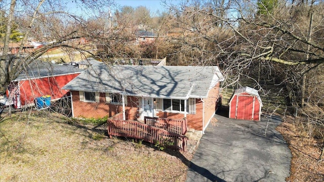 view of front facade featuring a porch, a storage unit, brick siding, and an outdoor structure