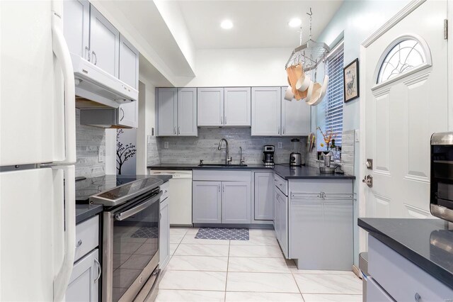 kitchen with dark countertops, backsplash, a sink, white appliances, and under cabinet range hood