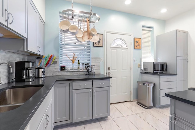 kitchen featuring dark countertops, stainless steel microwave, a sink, gray cabinetry, and backsplash