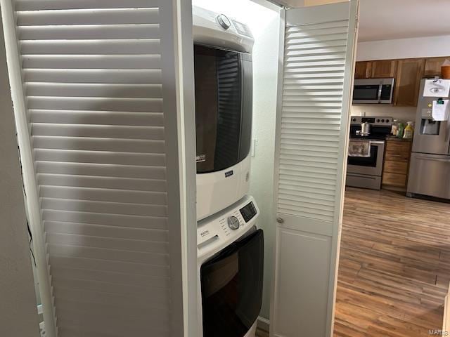 laundry area with wood finished floors, stacked washer and clothes dryer, and laundry area