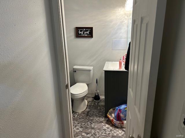 half bathroom with vanity, toilet, and baseboards