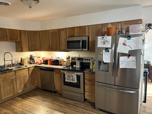 kitchen featuring stainless steel appliances, dark countertops, visible vents, a sink, and wood finished floors