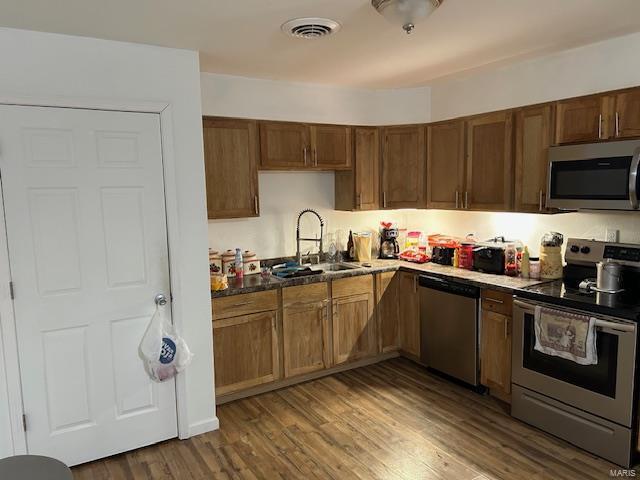 kitchen with stainless steel appliances, dark wood-style flooring, a sink, and visible vents