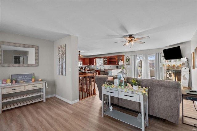 living area featuring a brick fireplace, ceiling fan, baseboards, and wood finished floors