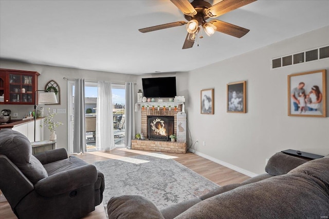 living area with a fireplace, visible vents, a ceiling fan, wood finished floors, and baseboards