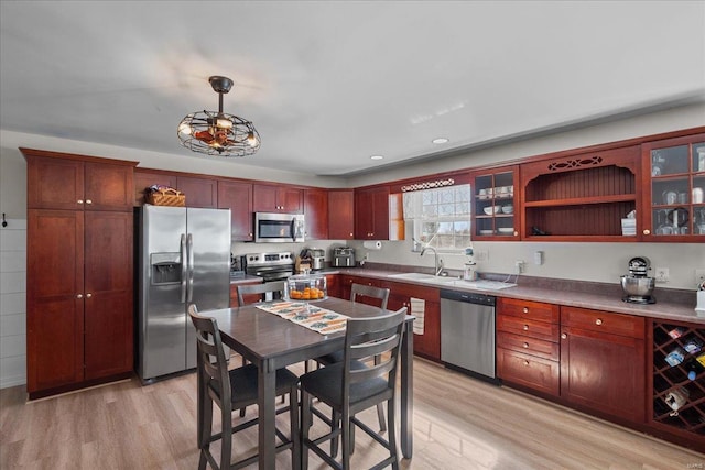 kitchen with glass insert cabinets, light wood finished floors, appliances with stainless steel finishes, and a sink