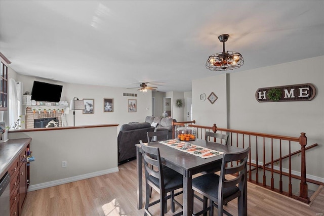 dining space featuring ceiling fan, visible vents, baseboards, a brick fireplace, and light wood finished floors