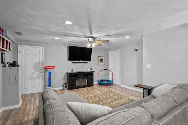 living room featuring baseboards, visible vents, a ceiling fan, a glass covered fireplace, and wood finished floors