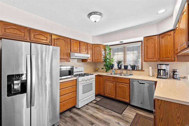 kitchen with under cabinet range hood, light countertops, appliances with stainless steel finishes, brown cabinetry, and a sink