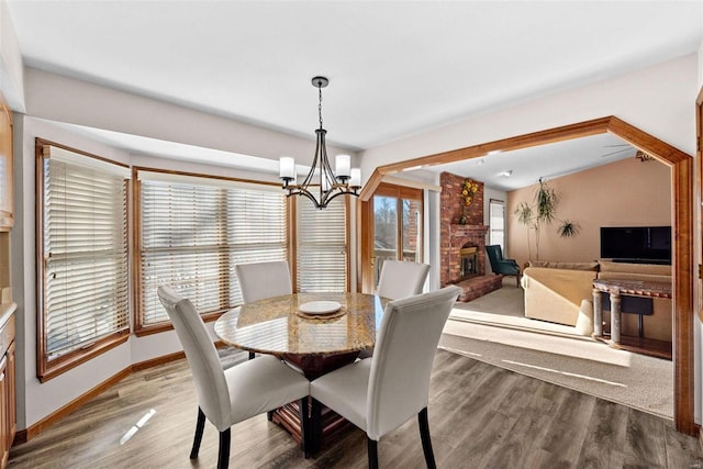 dining room featuring a chandelier, a fireplace, baseboards, and wood finished floors