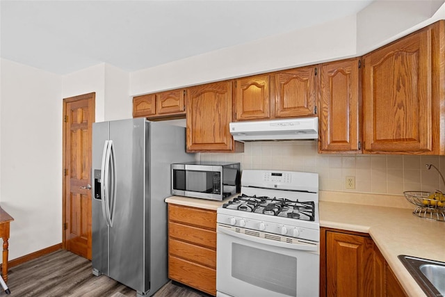 kitchen with brown cabinetry, stainless steel appliances, light countertops, under cabinet range hood, and tasteful backsplash