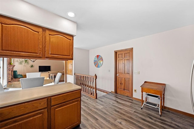 kitchen featuring baseboards, light countertops, recessed lighting, brown cabinets, and dark wood-style floors