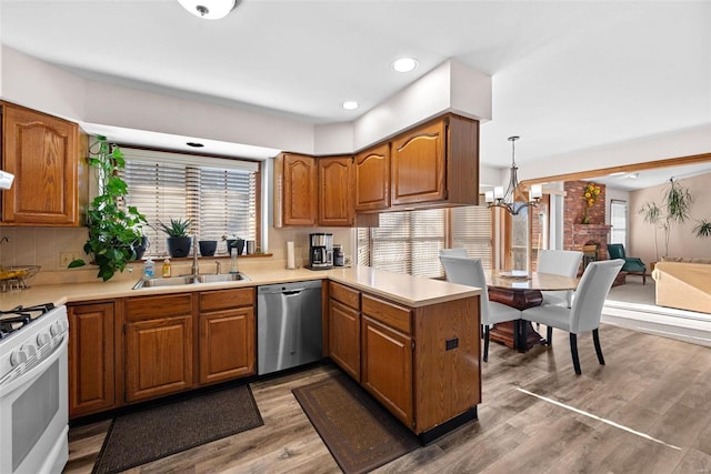 kitchen with white range with gas cooktop, brown cabinets, a sink, a peninsula, and dishwasher