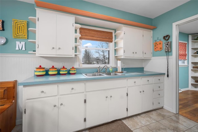 kitchen with open shelves, a wainscoted wall, white cabinetry, and a sink